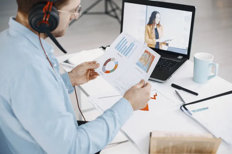 A man reviewing printed charts while on a video call with a colleague