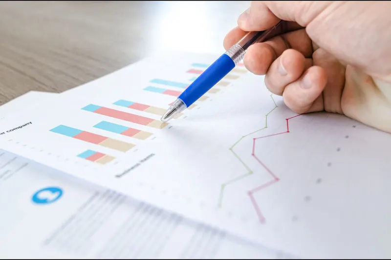 Close-up of a hand with a pen reviewing figures on printed charts
