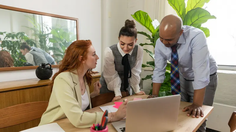 Three colleagues talking through work around a laptop in a bright office