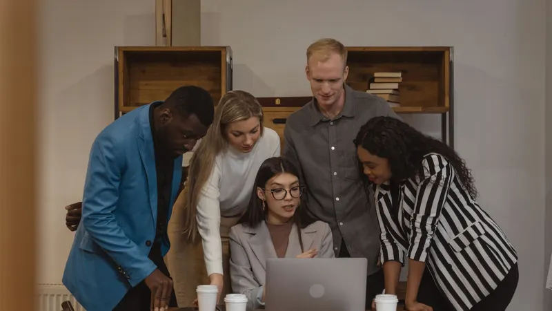 Five colleagues gathered around a laptop on a desk, planning work together