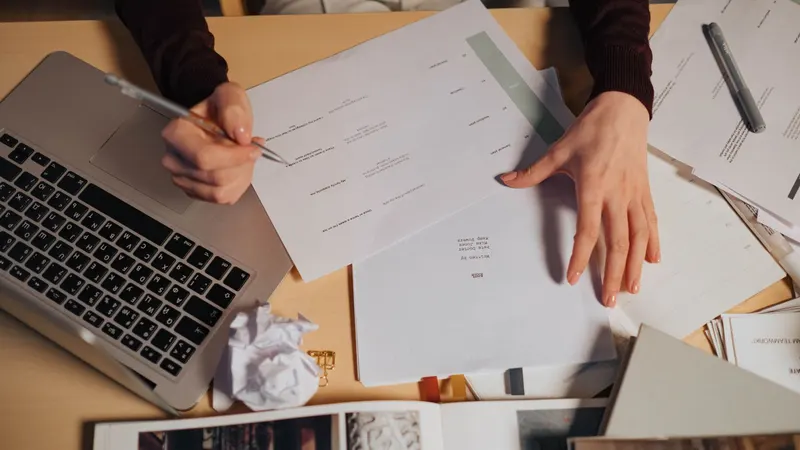 Overhead view of a person comparing printed documents beside a laptop and notebook